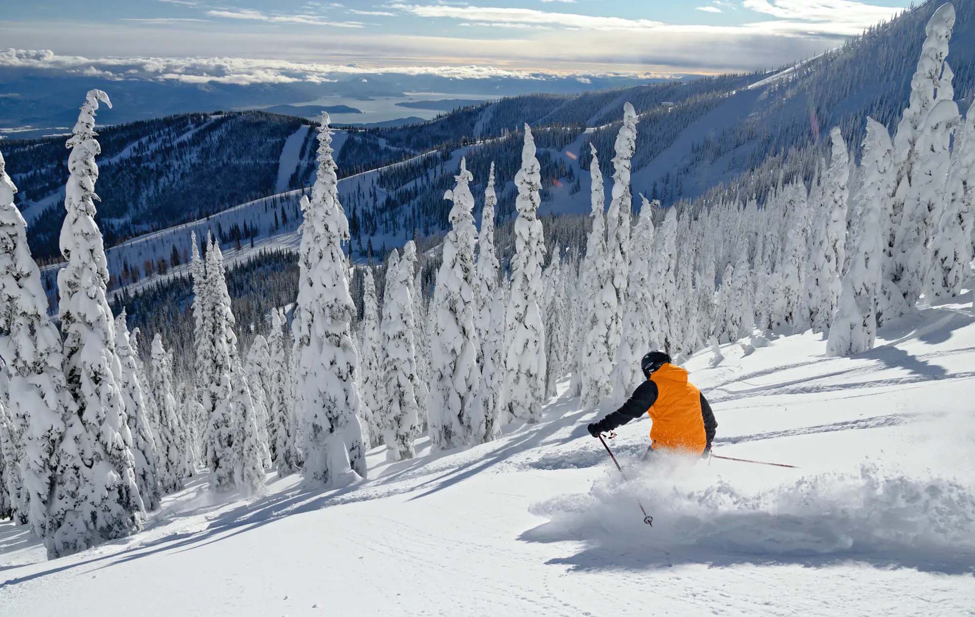 Skier carving fresh powder at Schweitzer Mountain with snow ghosts and Lake Pend Oreille
